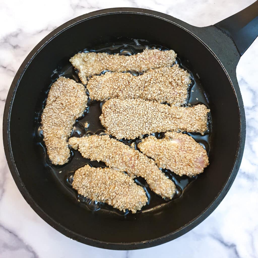 Uncooked sesame chicken strips in a frying pan.