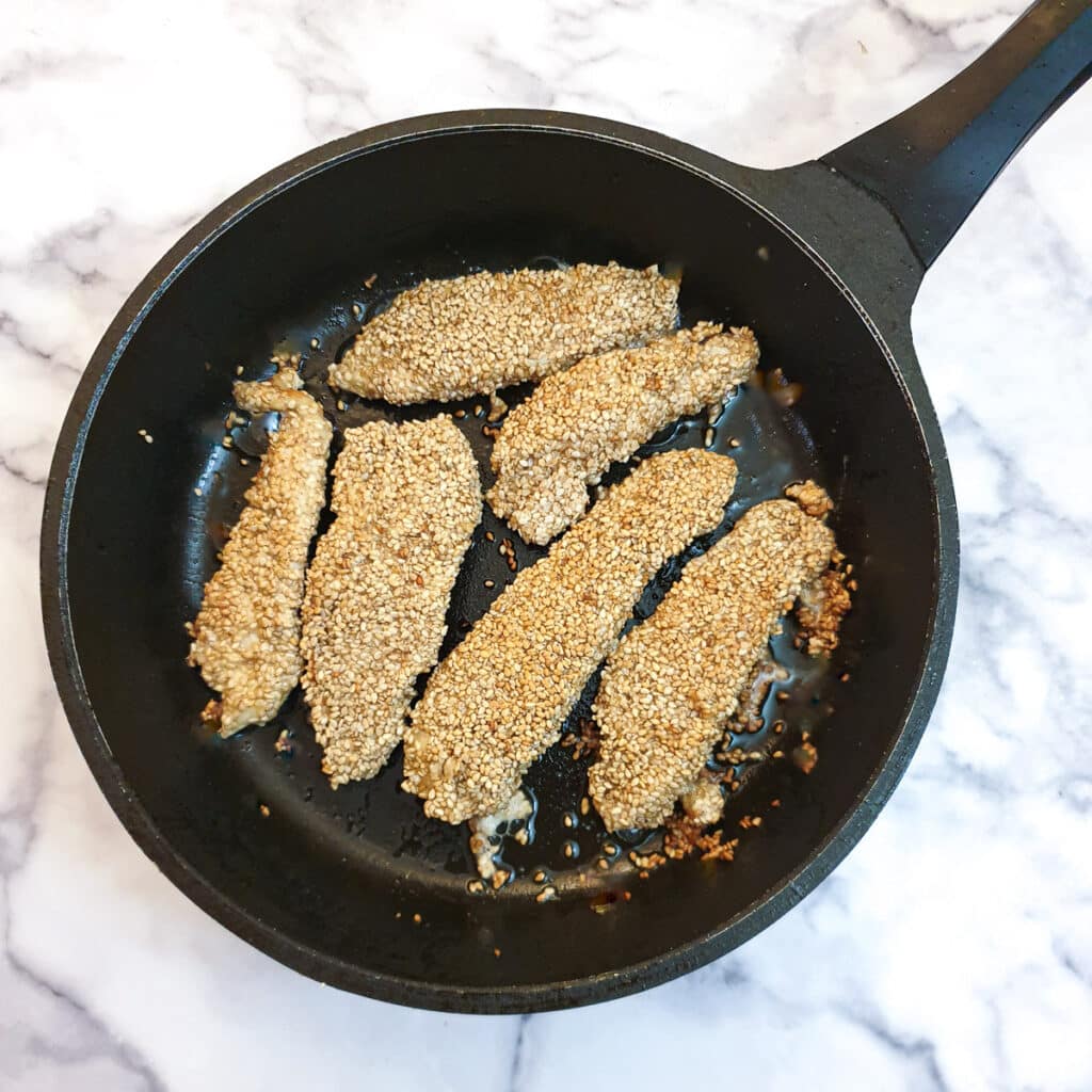 Browned sesame chicken strips in a frying pan.