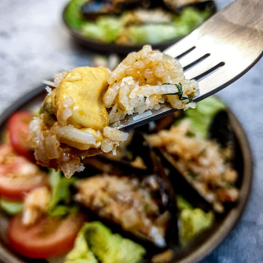 Close up of a mussel with rice stuffing on a fork.