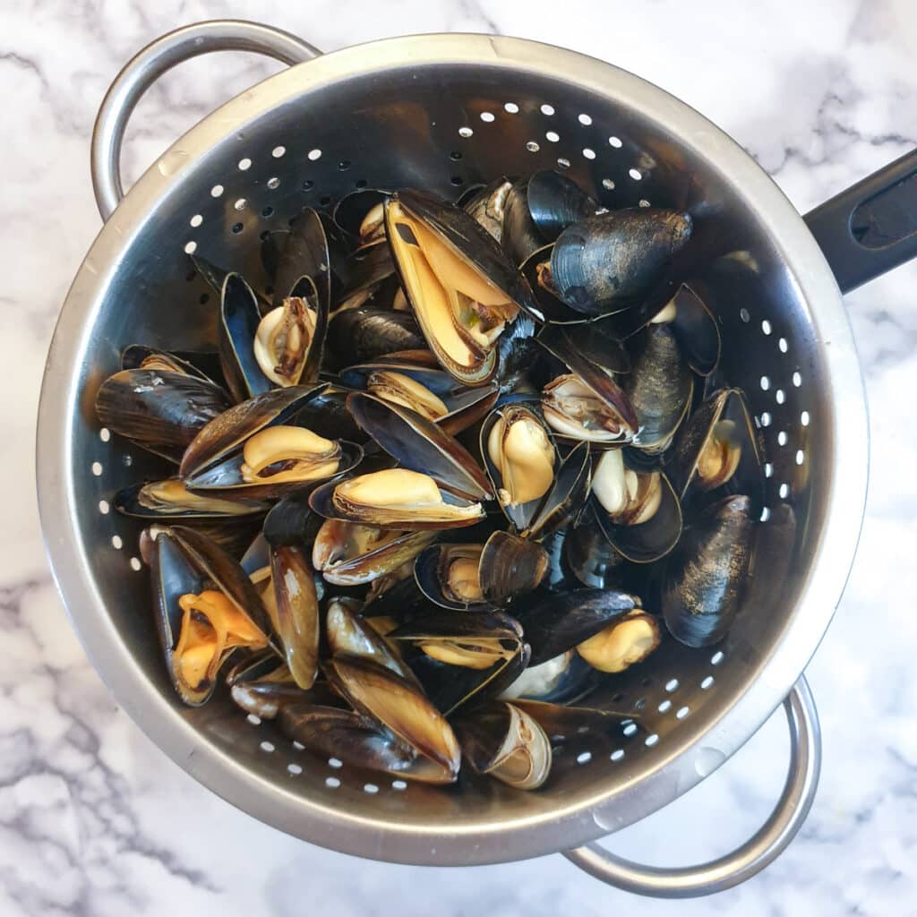 A colander filled with cooked mussels in their shells.