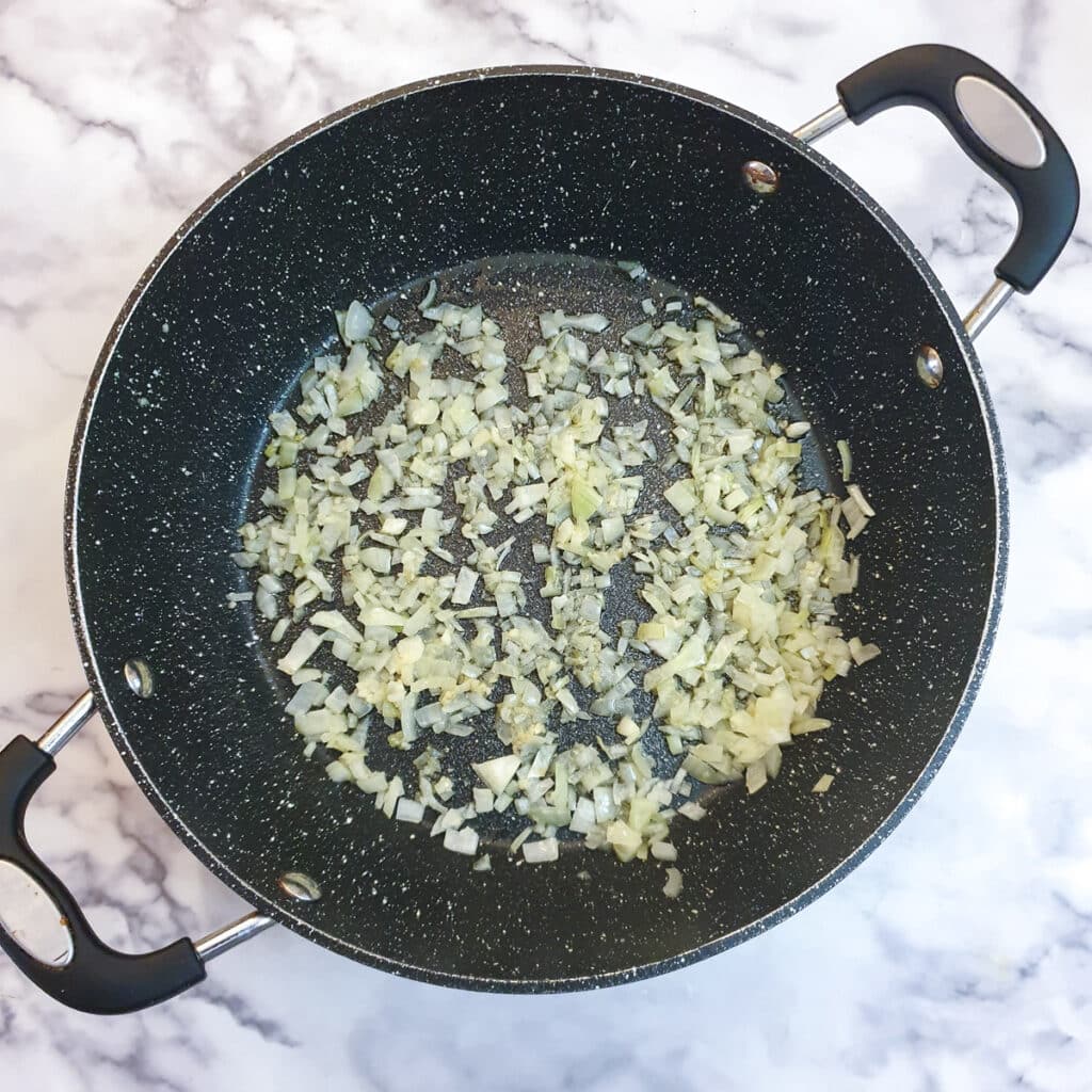 Chopped onions being softened in a large frying pan.