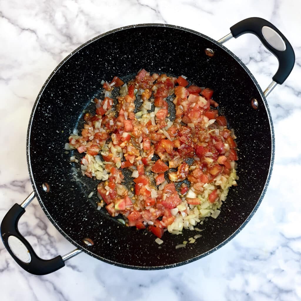 Chopped tomatoes added to onions in a frying pan.