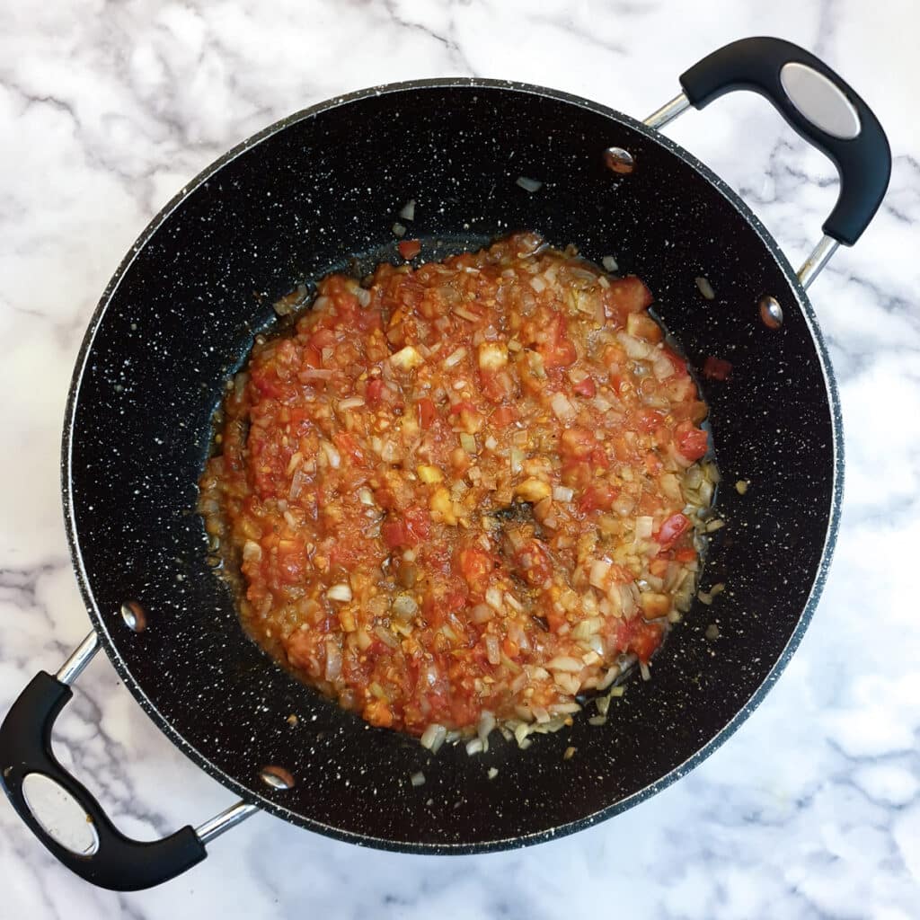 Cooked tomatoes and onions in a frying pan.