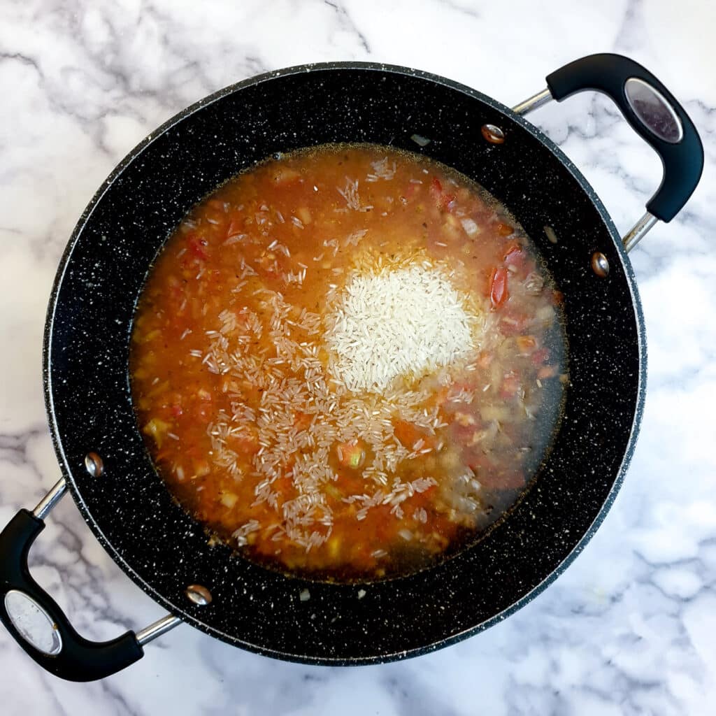 Water, rice and spices added to onions and tomatoes in a frying pan.