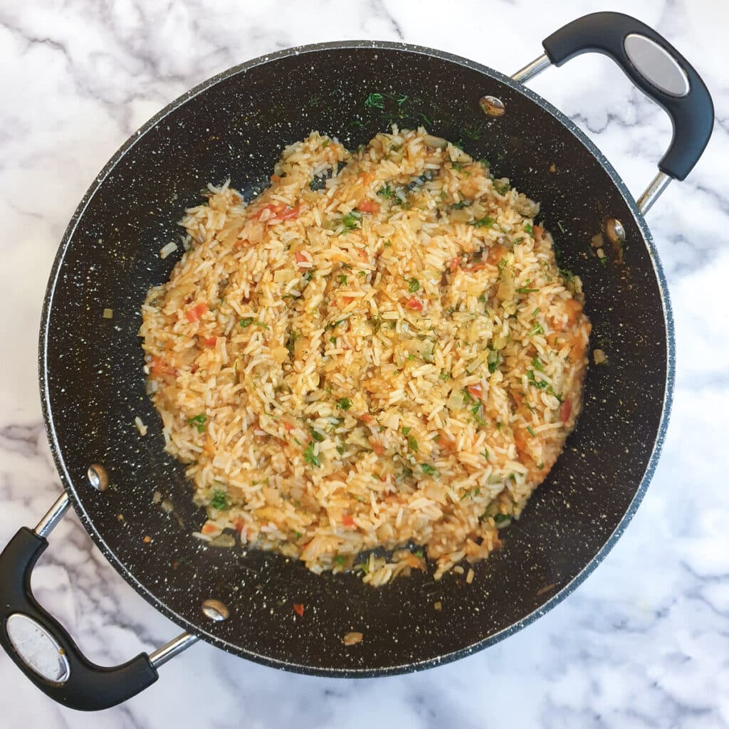 Cooked tomato rice in a frying pan with chopped fresh herbs stirred through.
