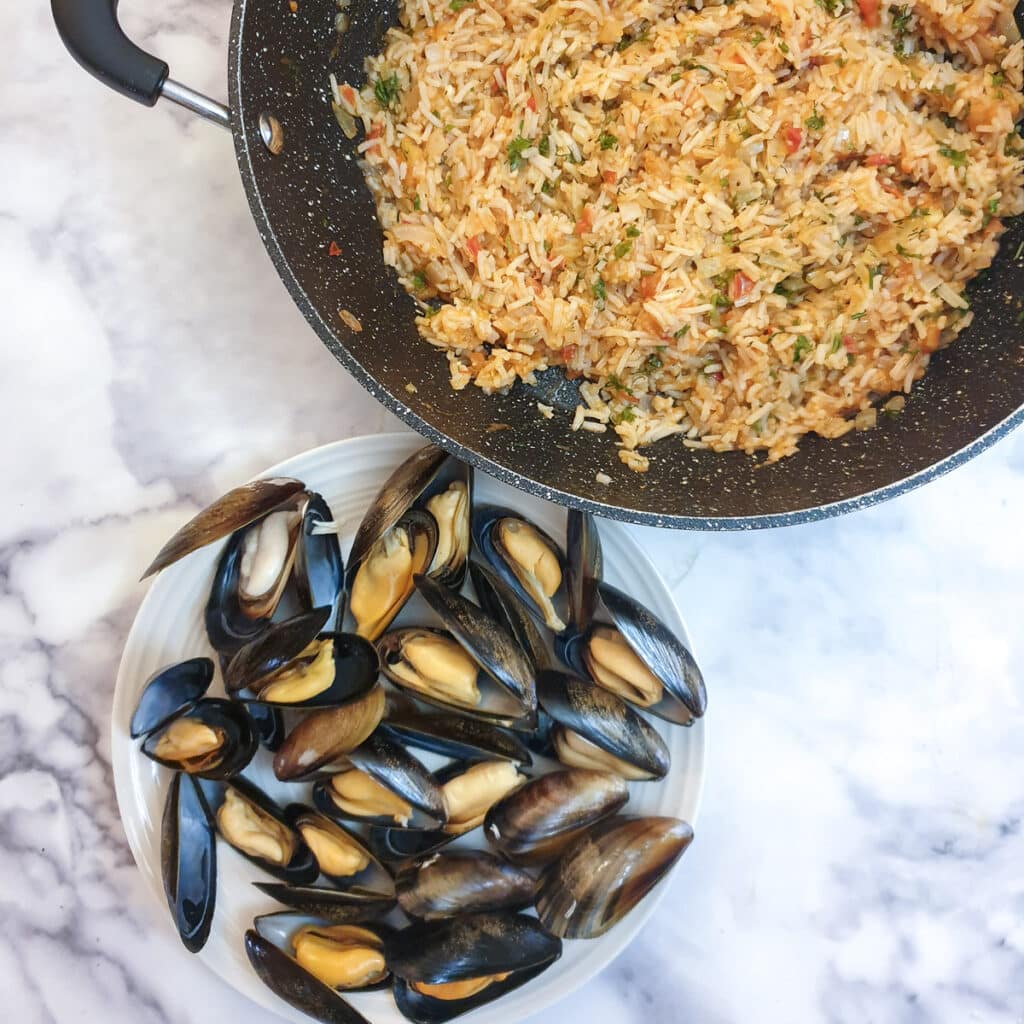 A pan of tomato rice next to a plate of cooked mussels.