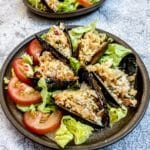 5 stuffed mussels on a brown plate garnished with shredded lettuce and sliced tomatoes.