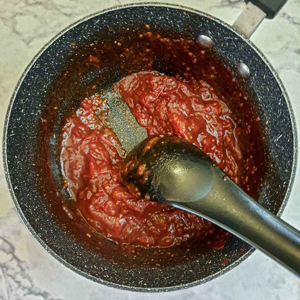 Tomato jam in a saucepan showing how a spatula can be drawn through the jam to leave a trail.