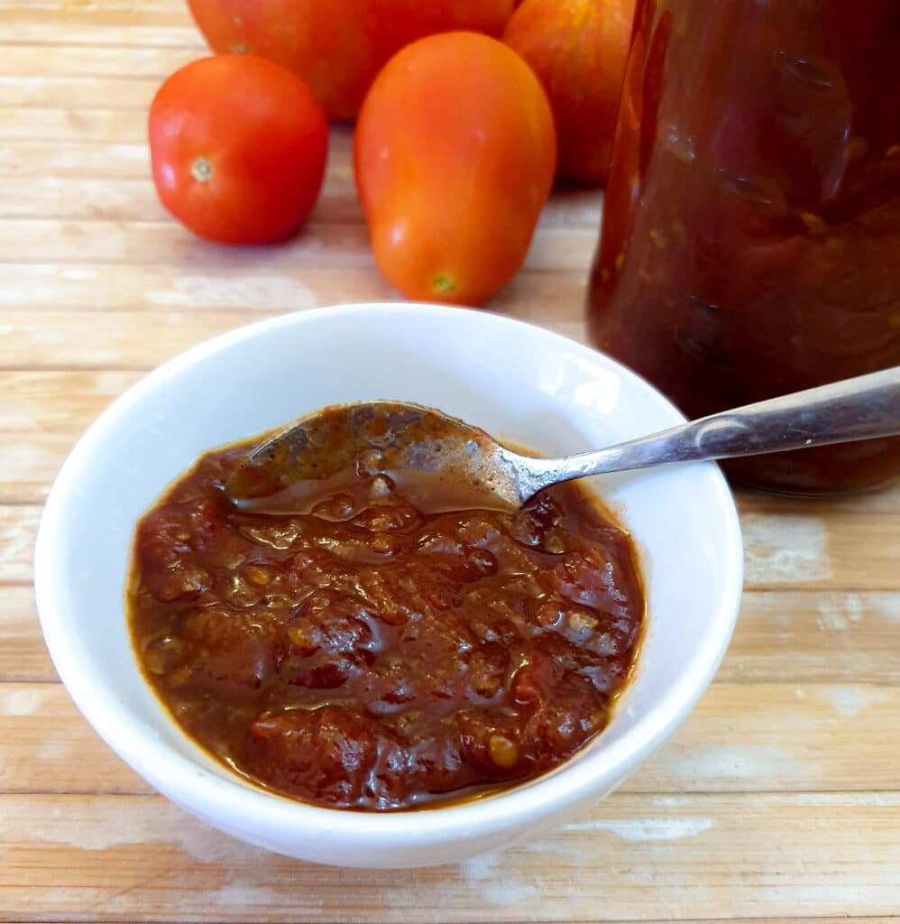 A small white dish filled with tomato jam, with a spoon.