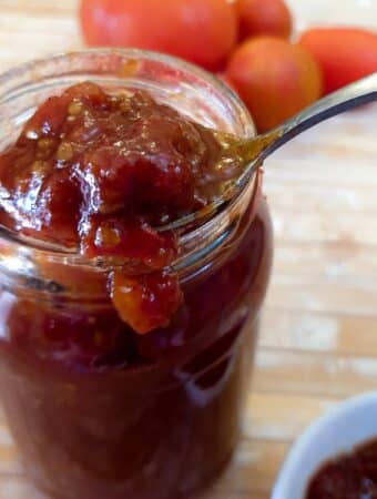 A jar of tomato jam with a spoonful being scooped out.