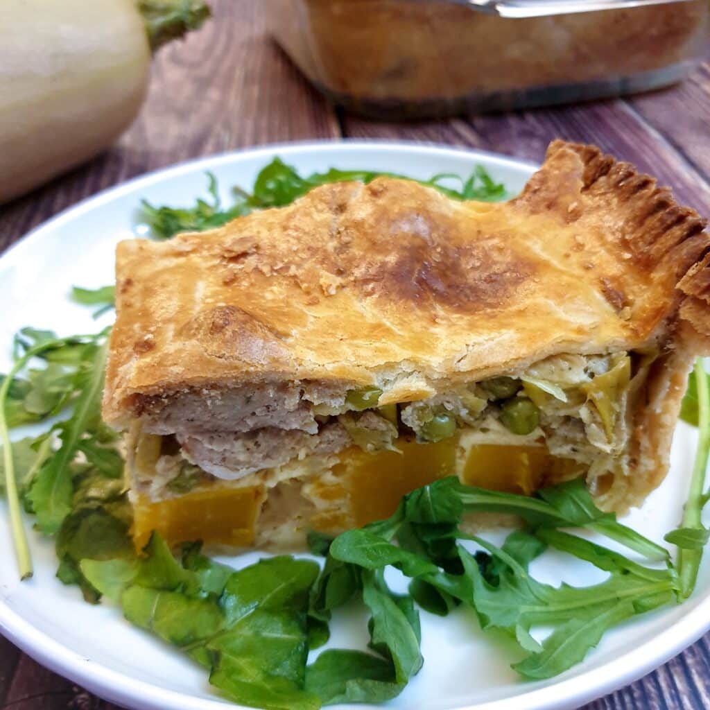 A slice of butternut, leek and sausage pie on a white plate.