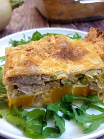 A slice of butternut, leek and sausage pie on a white plate.