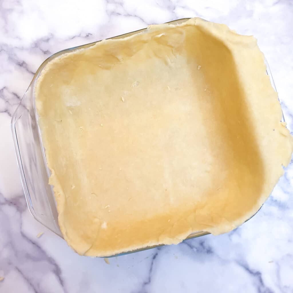 A glass baking dish lined with raw pastry.