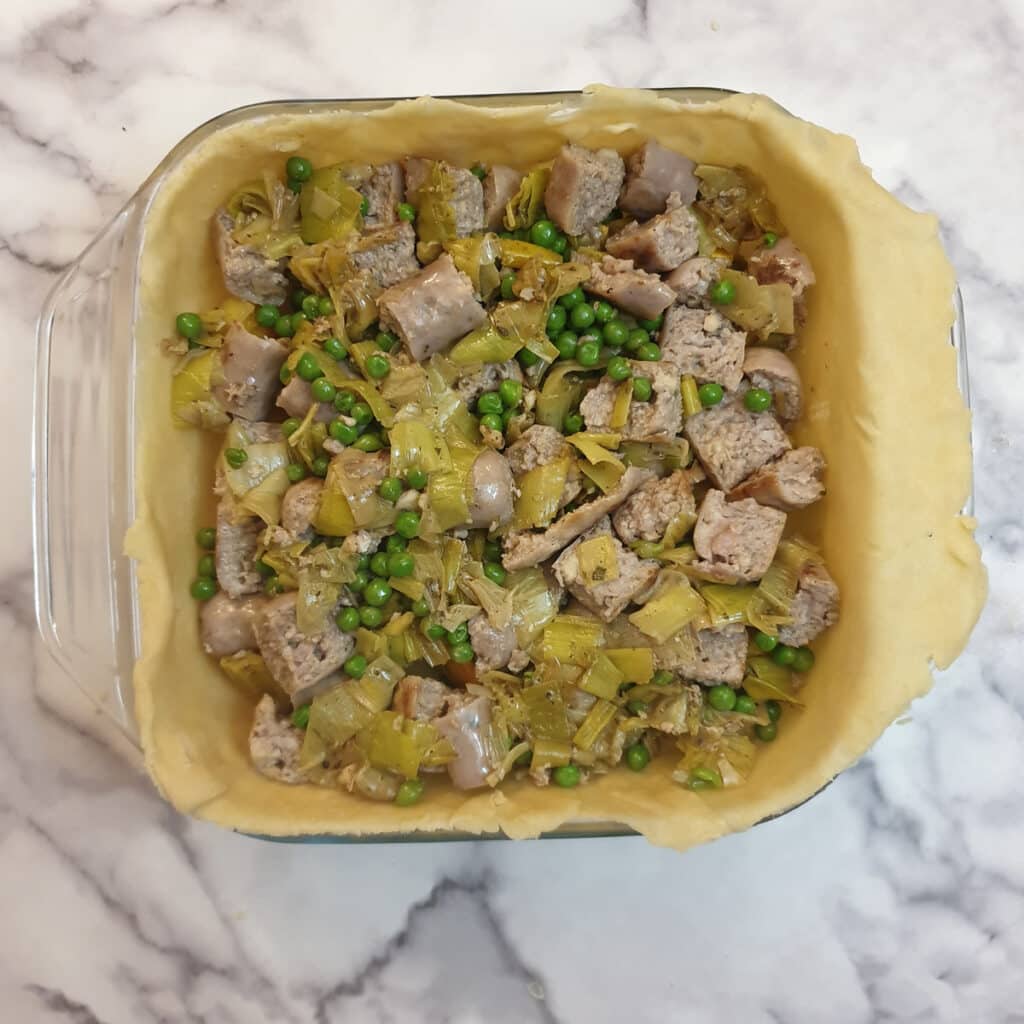 Sausages, peas and leeks covering pieces of butternut in an unbaked pastry shell.