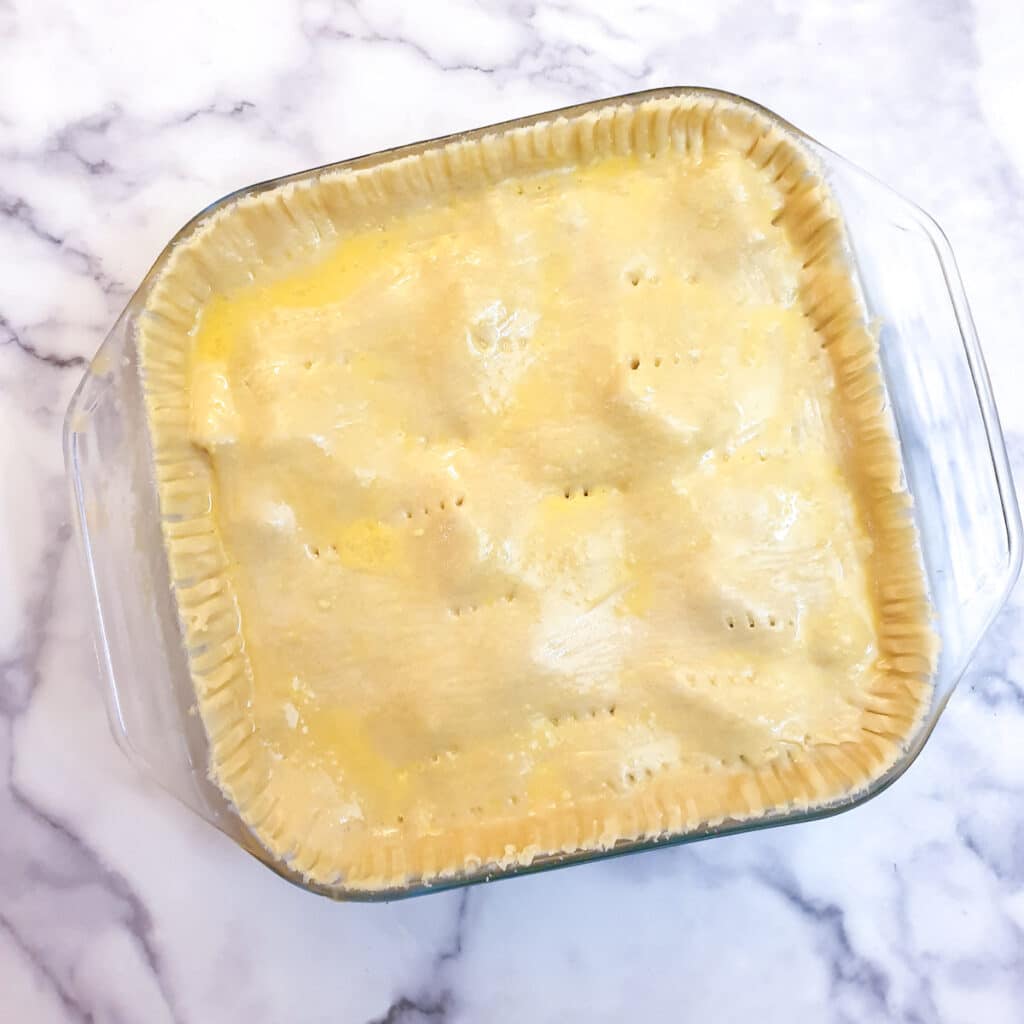 An unbaked butternut, leek and sausage pie in a glass baking dish.