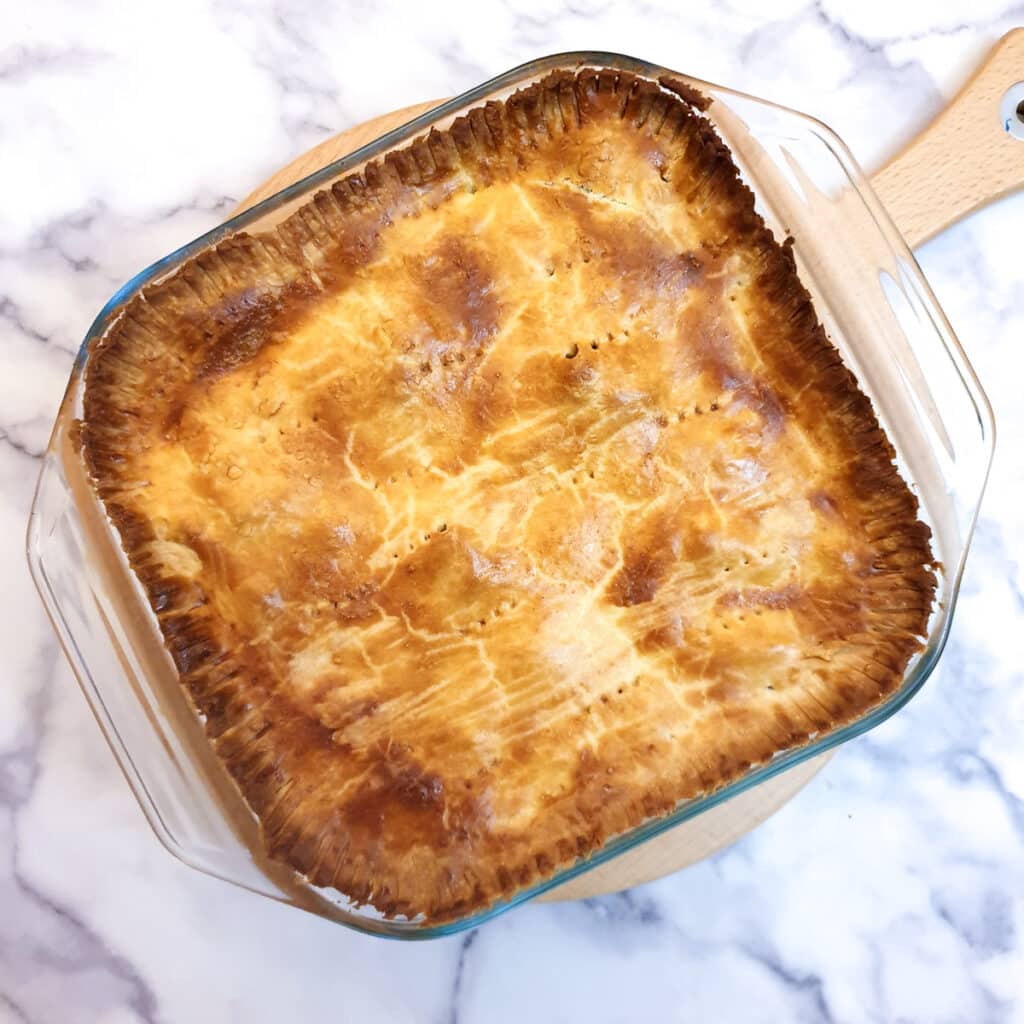 A baked butternut, leek and sausage pie in a glass baking dish.