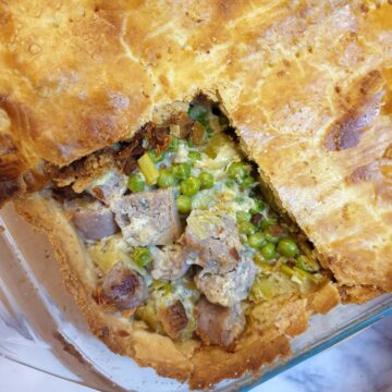 Overhead shot of butternut, leek and sausage pie,, with a corner of the pastry removed to show the filling.
