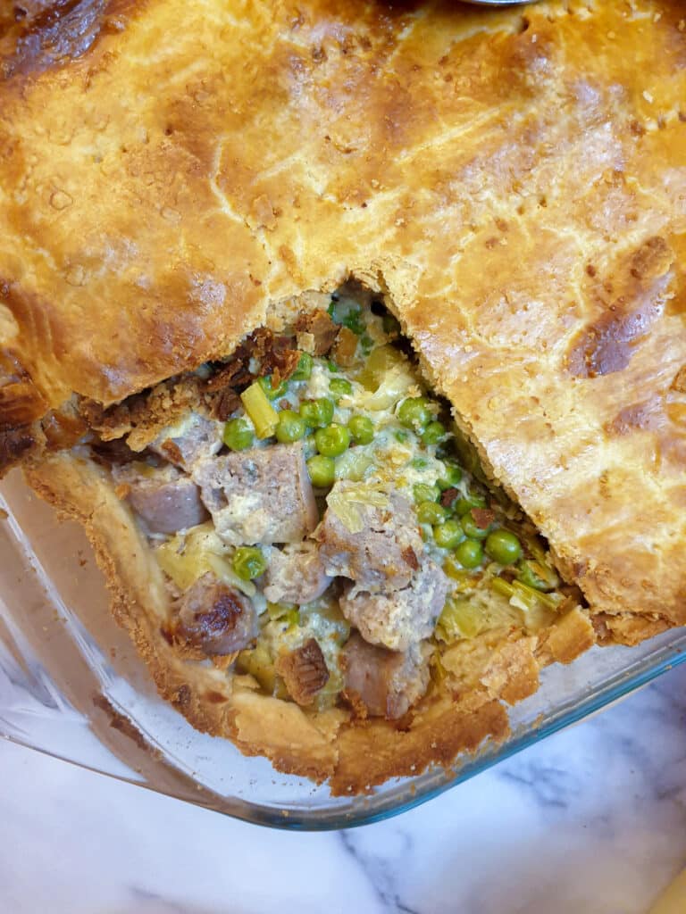 Overhead shot of butternut, leek and sausage pie,, with a corner of the pastry removed to show the filling.