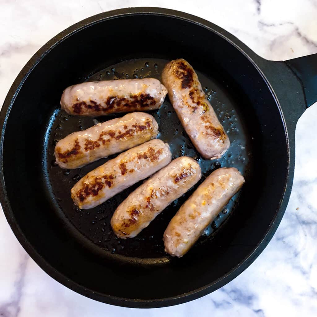 6 sausages being browned in a frying pan.