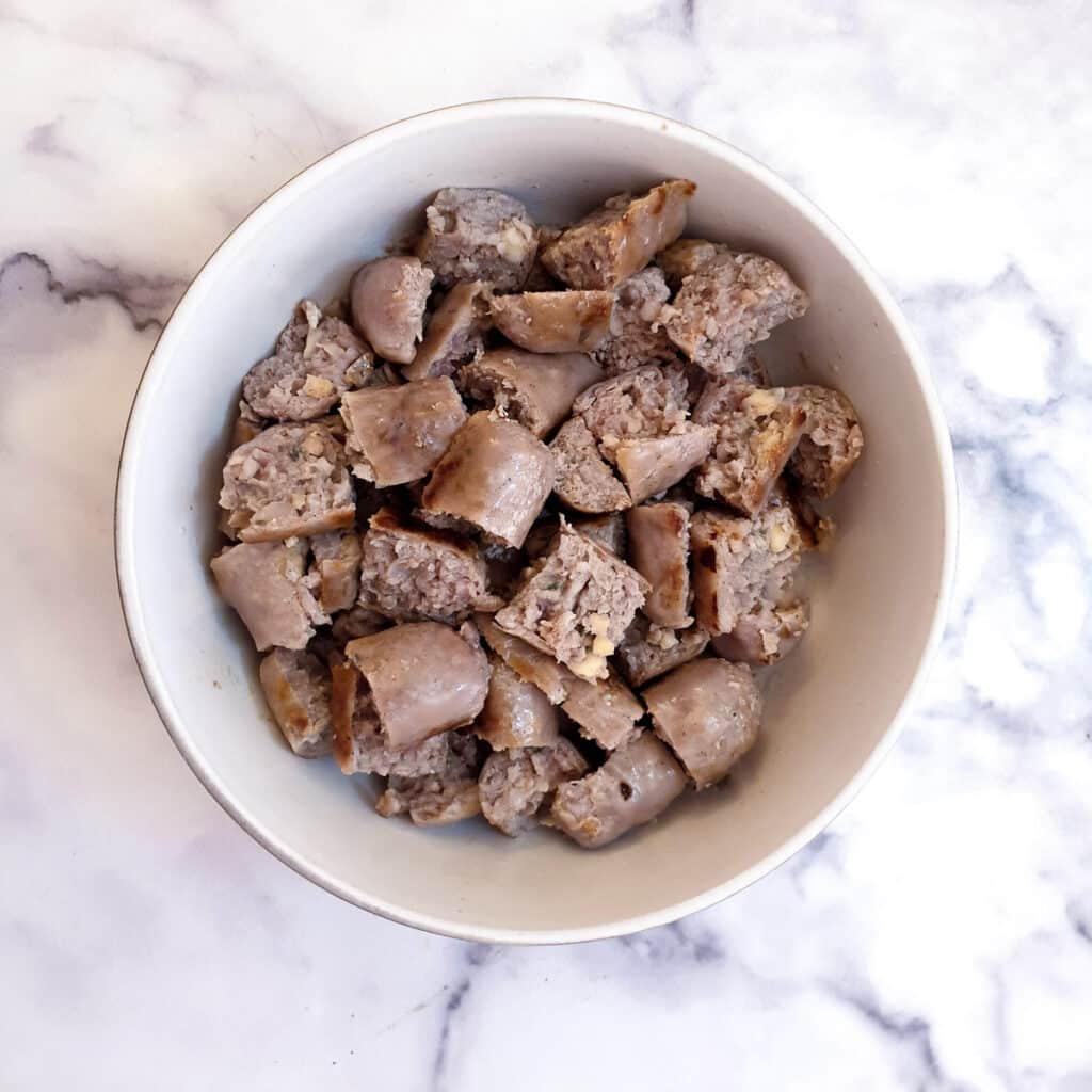 A small white bowl holding pieces of chopped sausages.