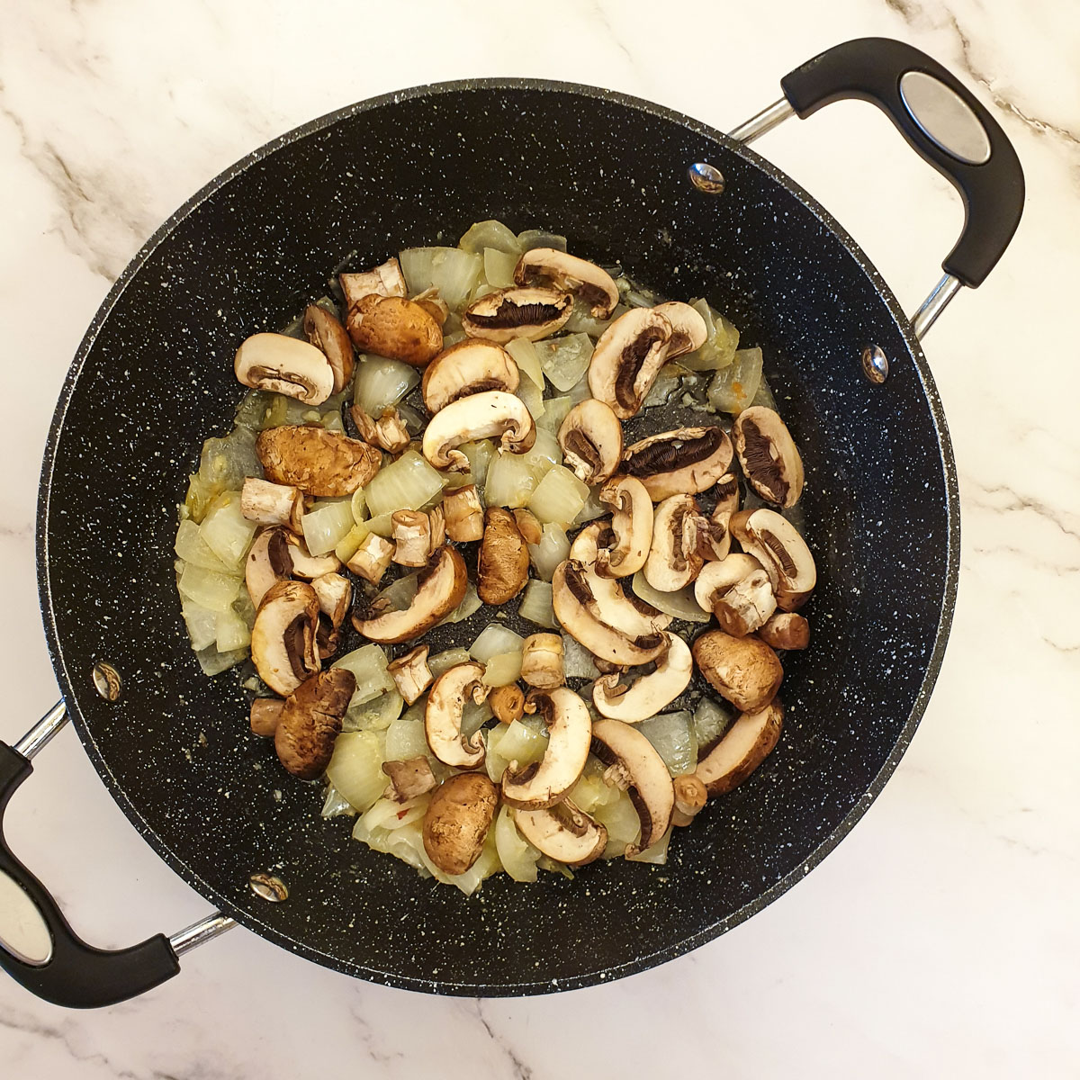 Mushrooms added to onions in a frying pan.