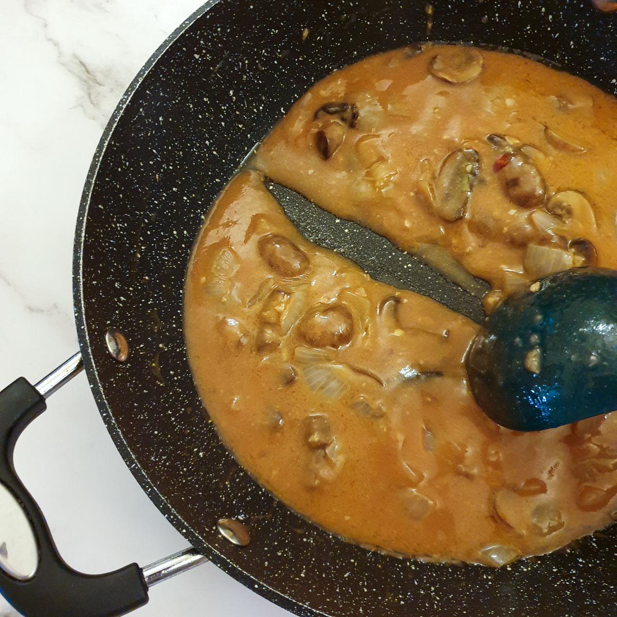 A spoon drawing a trail through a pan of diane sauce.