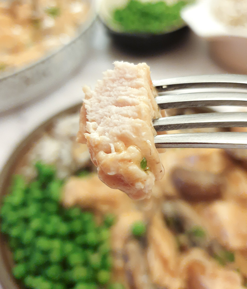 A close up of a piece of chicken on a fork held over a plate of chicken Diane, showing how moist and juicy the chicken is.