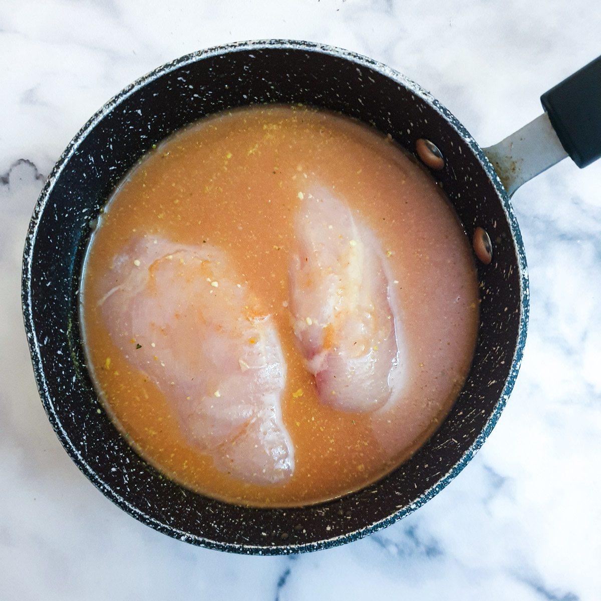 2 chicken breasts covered with stock in a small black saucepan.