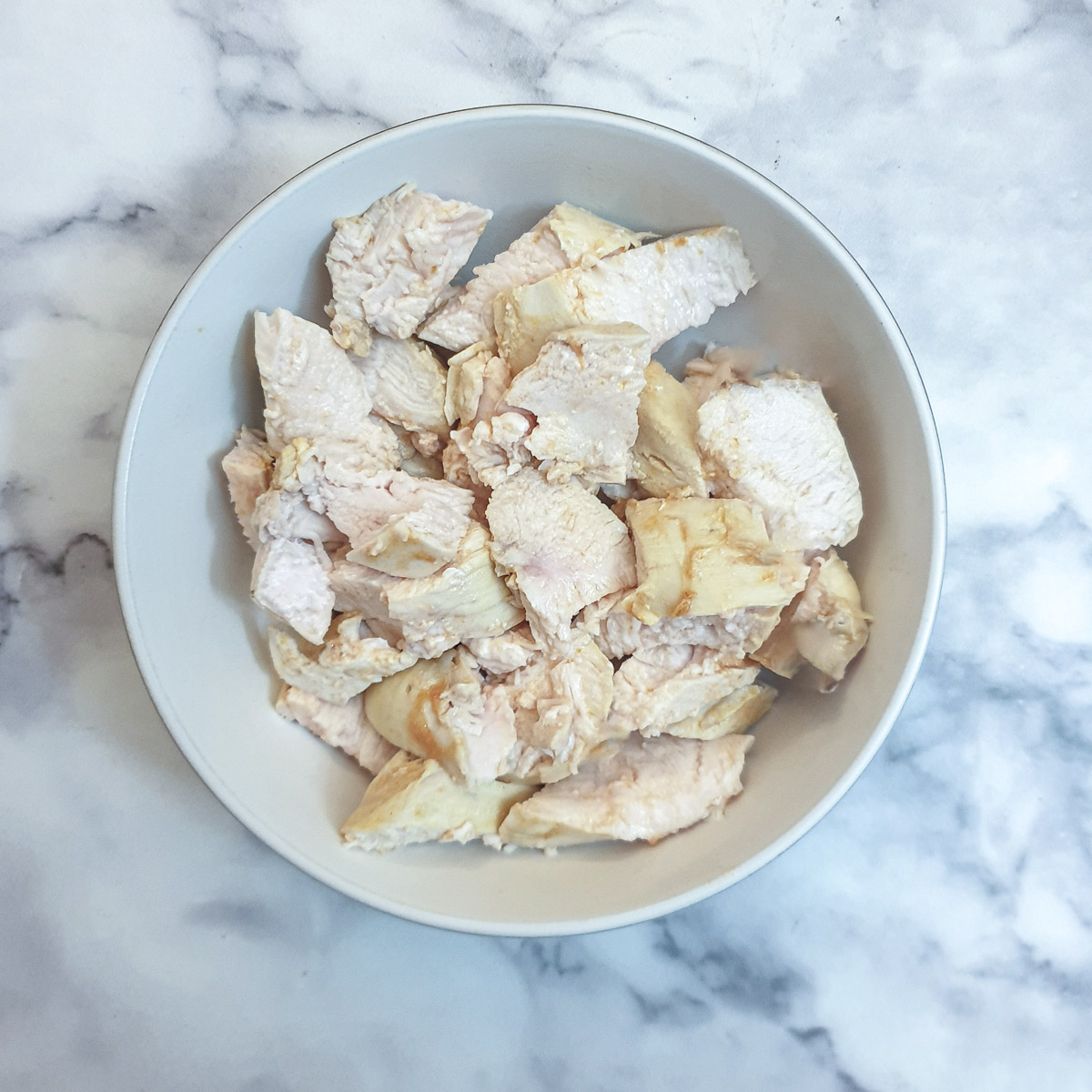 A white bowl containing bite-sized pieces of poached chicken breast.