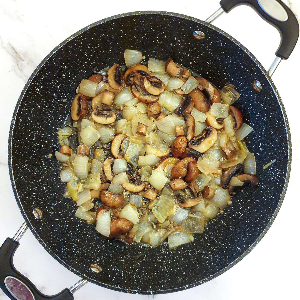 Cooked mushrooms and onions in a frying pan.