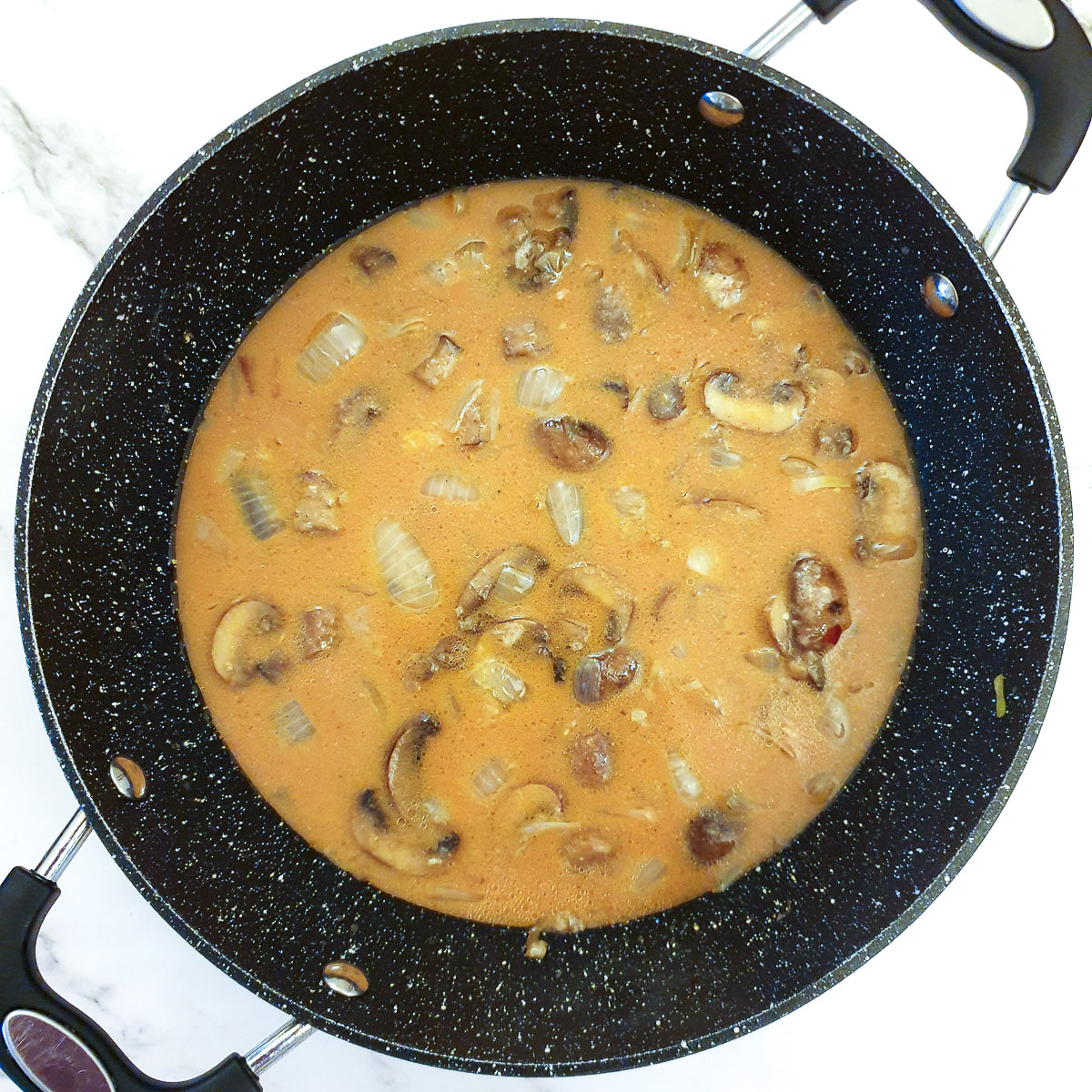 Sauce added to mushrooms and onions in a frying pan.