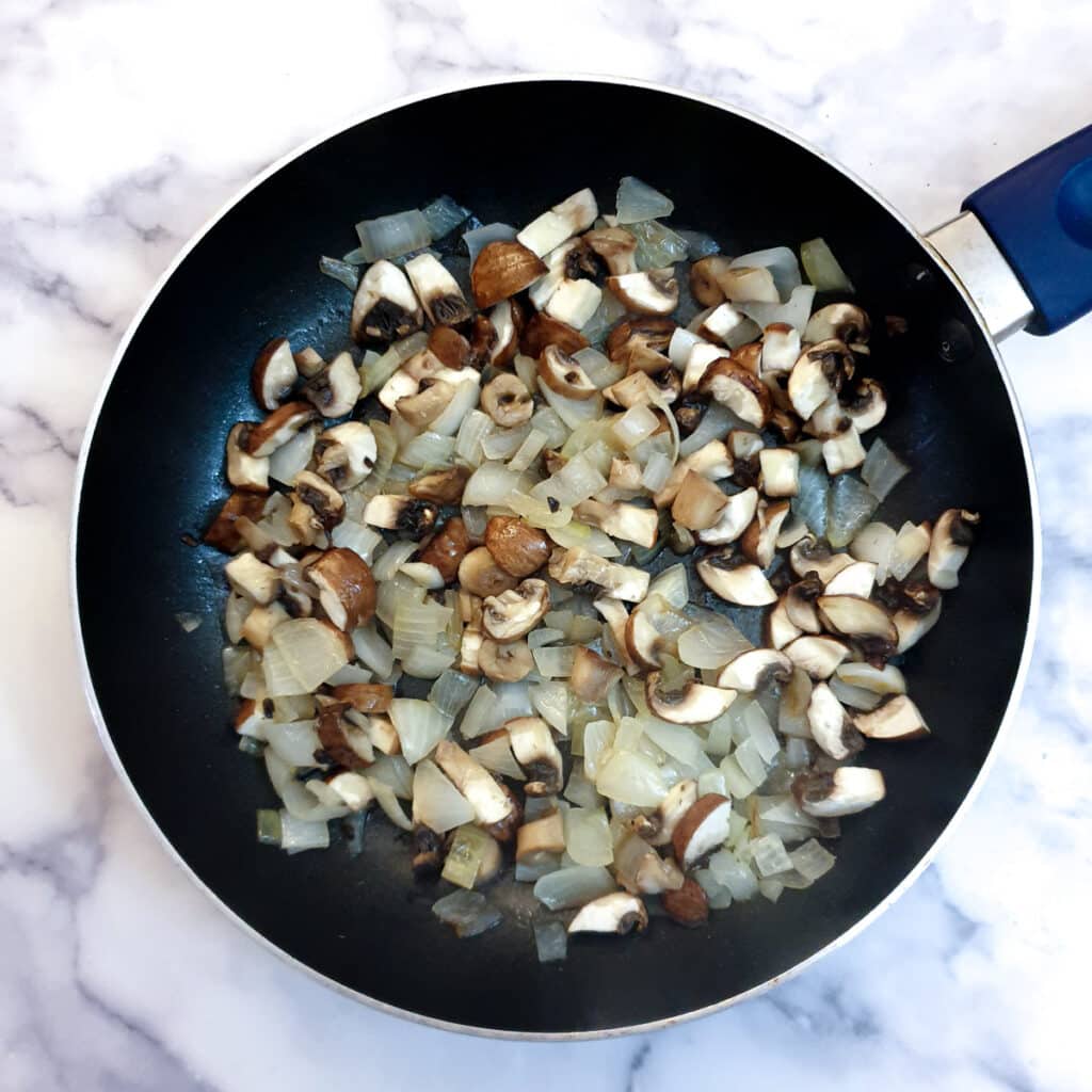 Mushrooms added to the onions in a frying pan.