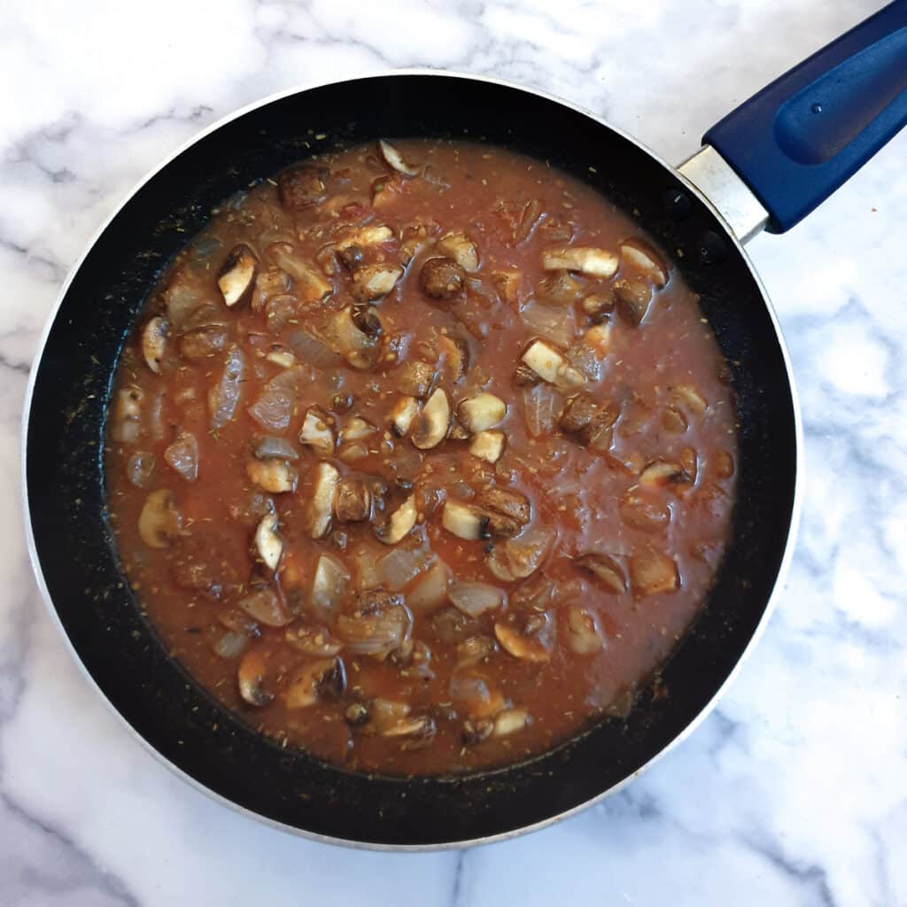 Passata added to mushrooms and onions in a frying pan.