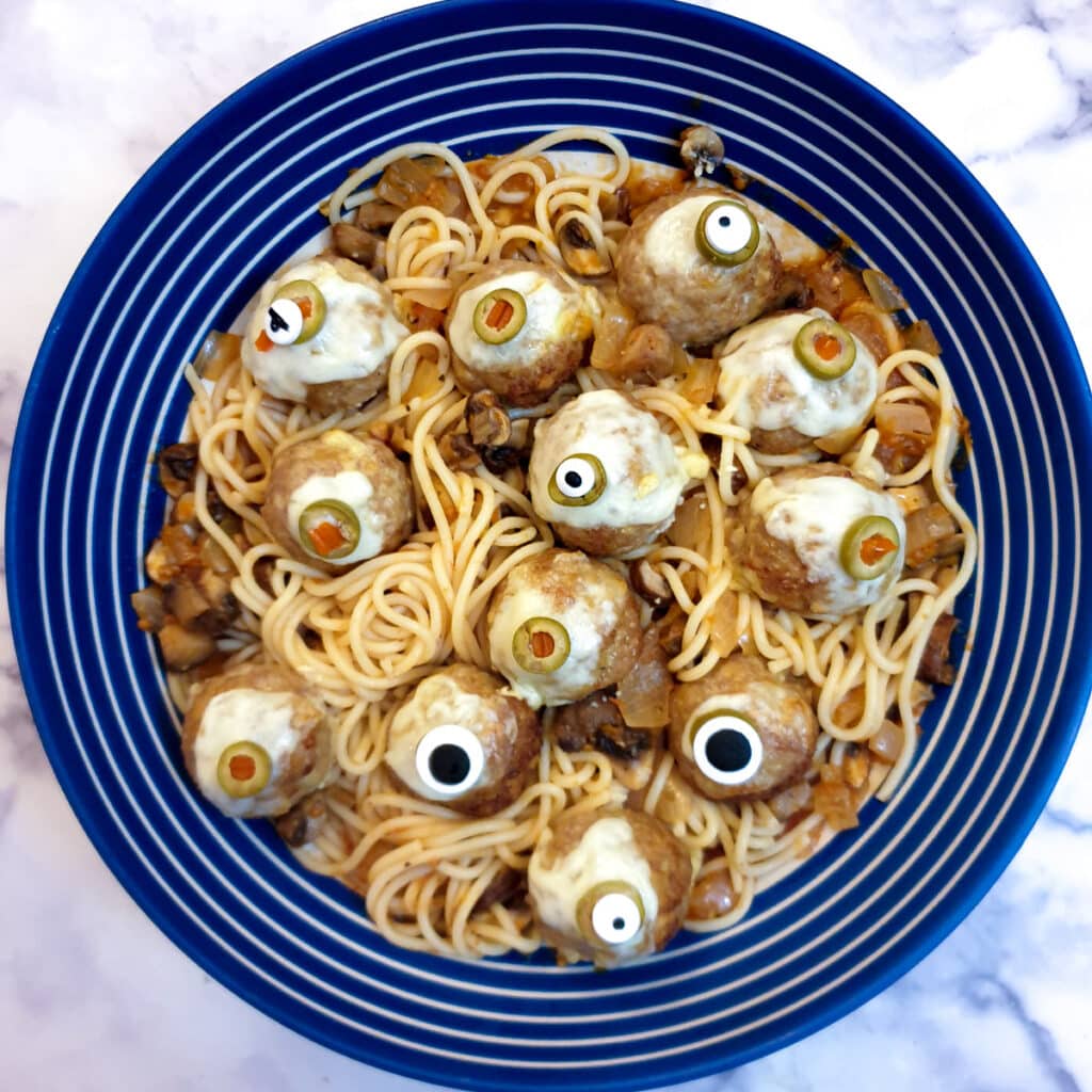 A blue and white striped serving dish filled with Halloween worms and eyeballs.