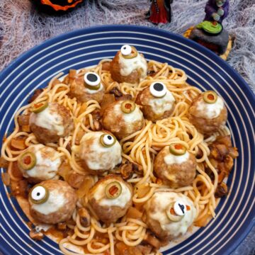 A blue and white striped serving dish filled with spaghetti in tomato sauce and topped with halloween eyeball meatballs.