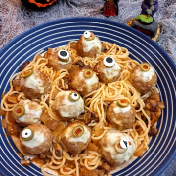 A blue and white striped serving dish filled with spaghetti in tomato sauce and topped with halloween eyeball meatballs.