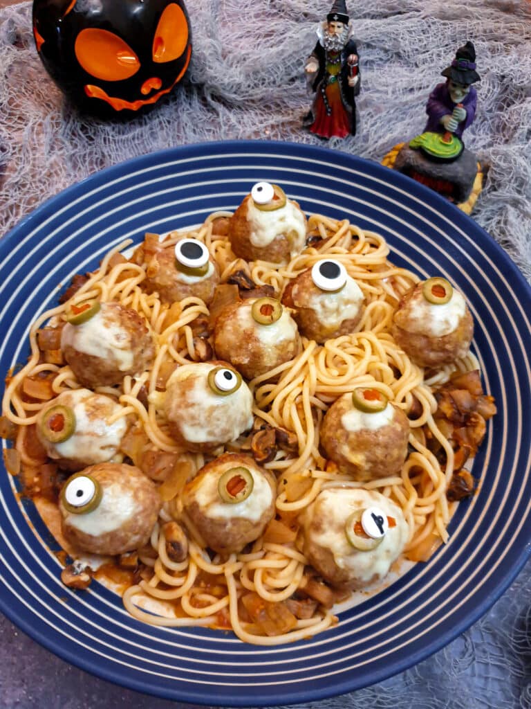 A blue and white striped serving dish filled with spaghetti in tomato sauce and topped with halloween eyeball meatballs.