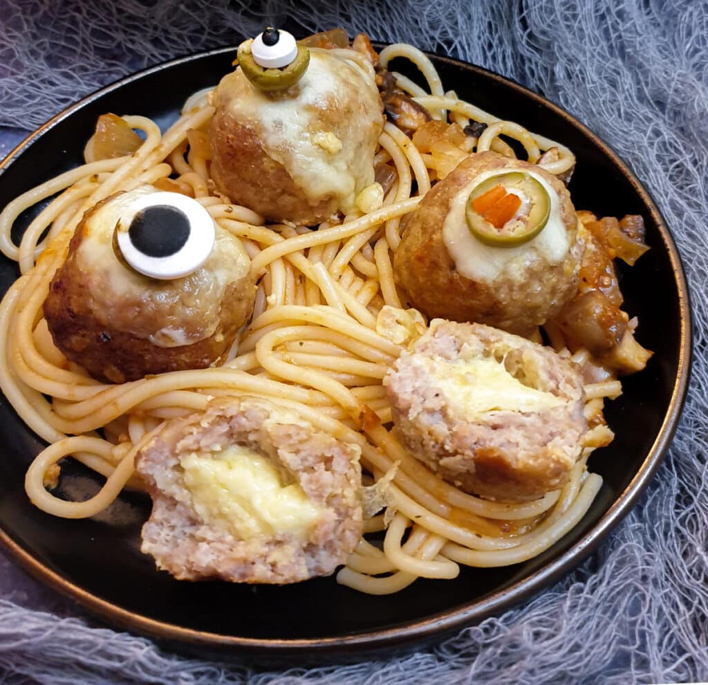 Meatballs on a bed of spaghetti with one meatball cut in half to show the cheese on the inside.