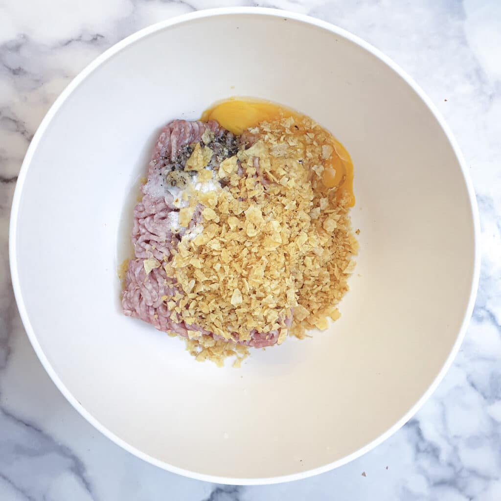 Pork mince, egg, salt, pepper and crushed crisps in a mixing bowl.