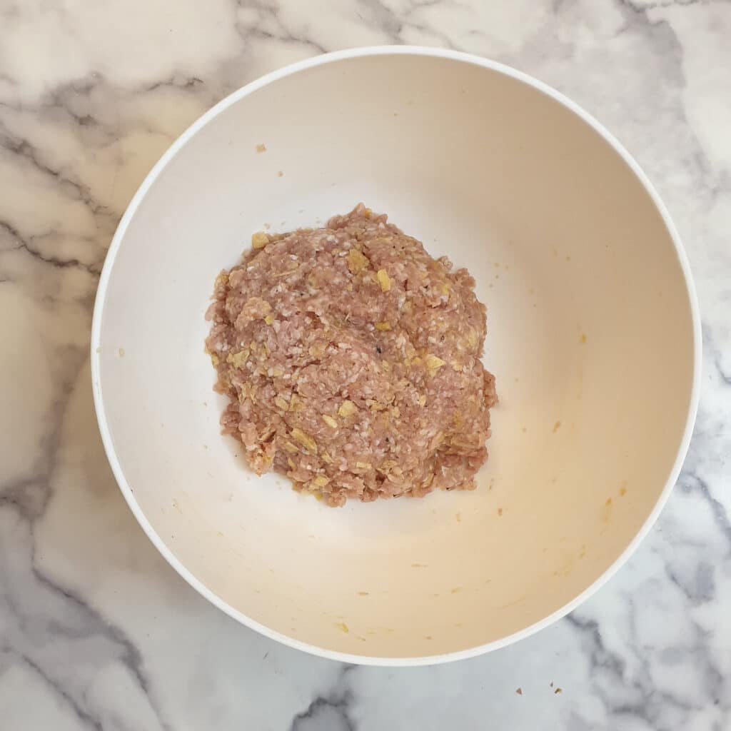 A white mixing bowl containing mixed meatball mixture.