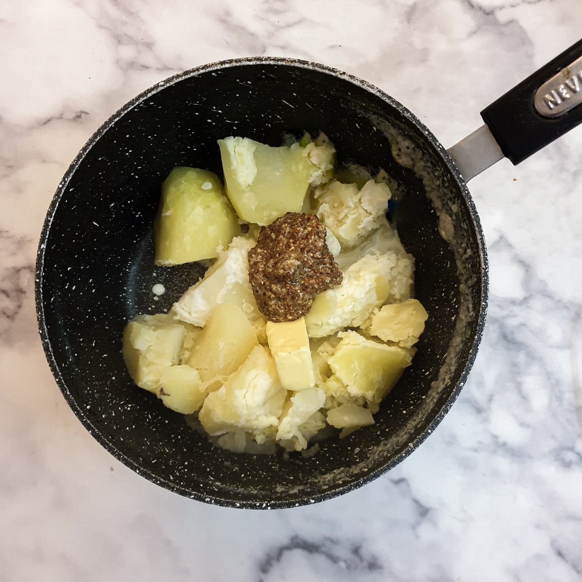 Boiled potatoes in a saucepan with cream, butter and wholegrain mustard.