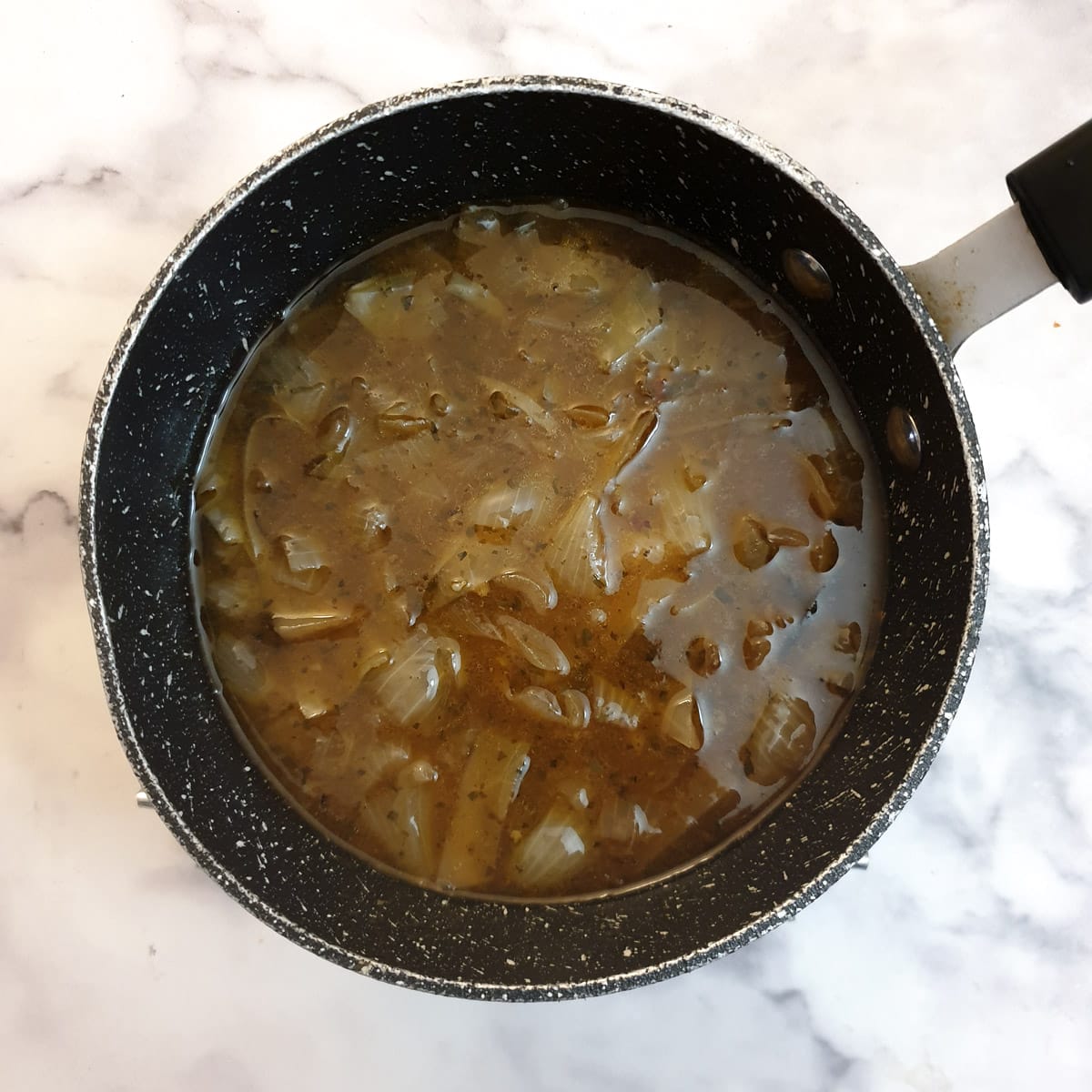 Lamb shank cooking liquid in a saucepan.