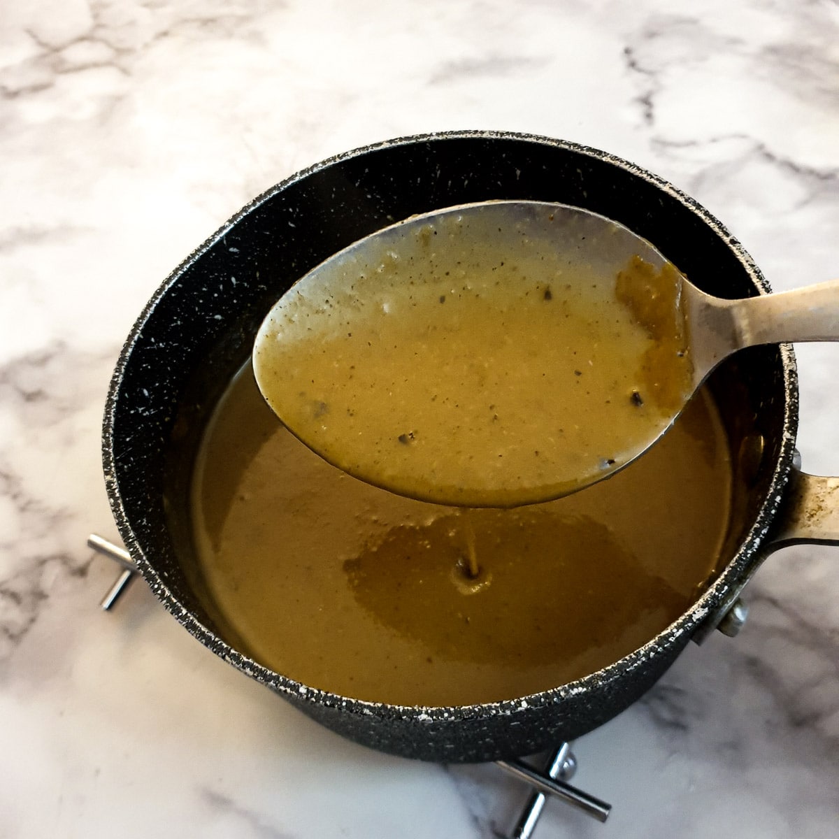 A spoon of smooth blended gravy held over a saucepan.