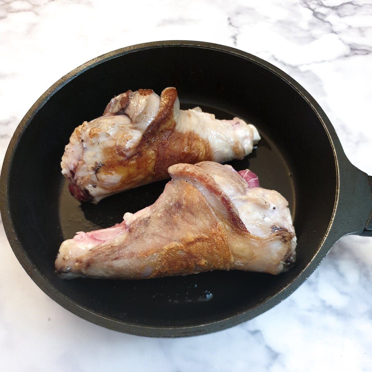Two lamb shanks browning in a frying pan.