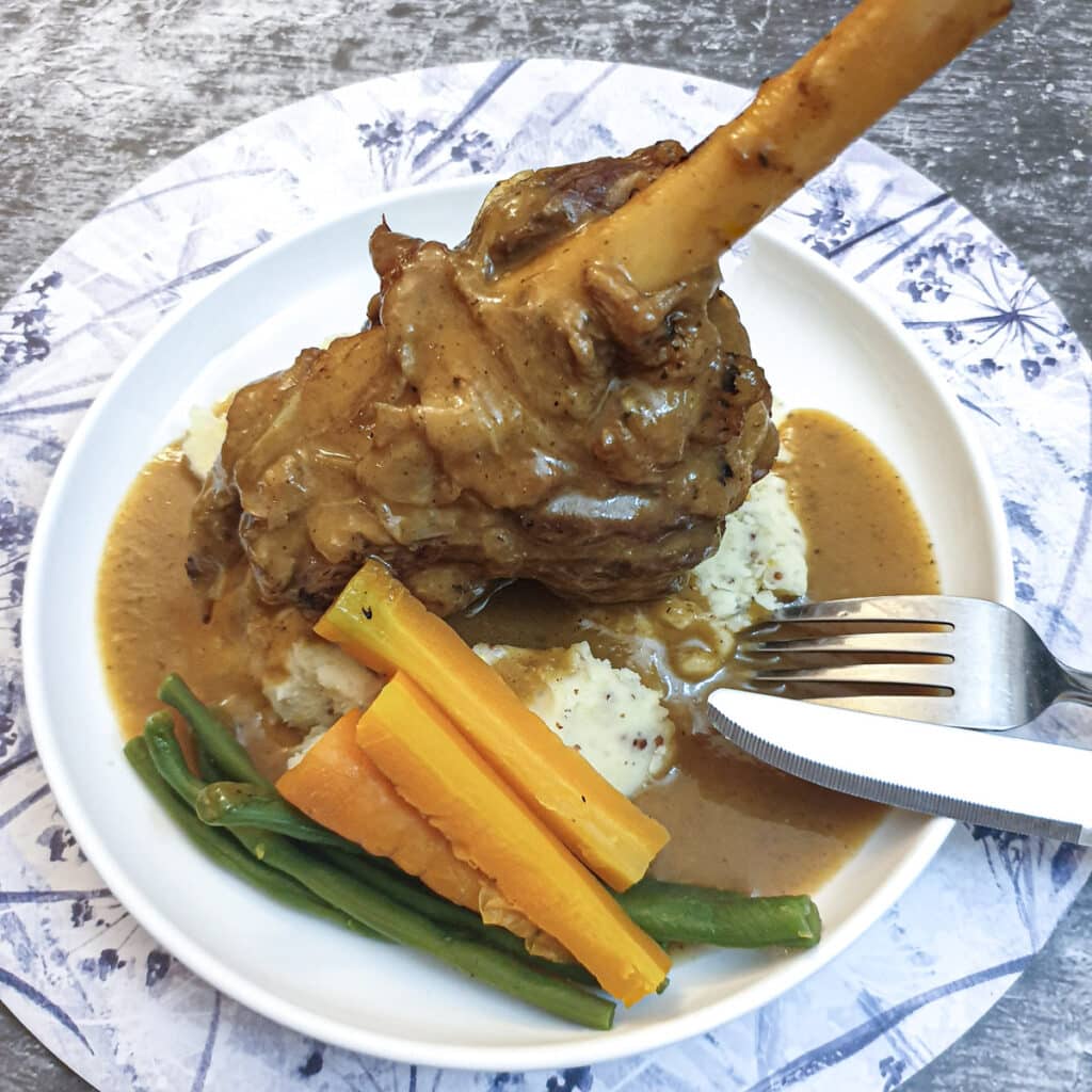 A minted lamb shank on a bed of mustard mashed potatoes.