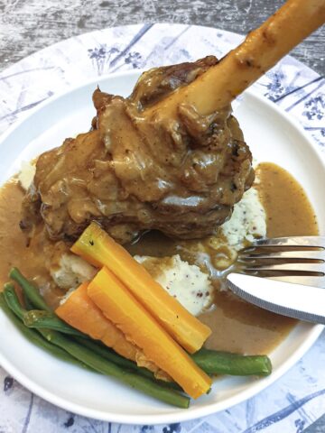 A minted lamb shank on a bed of mustard mashed potatoes.