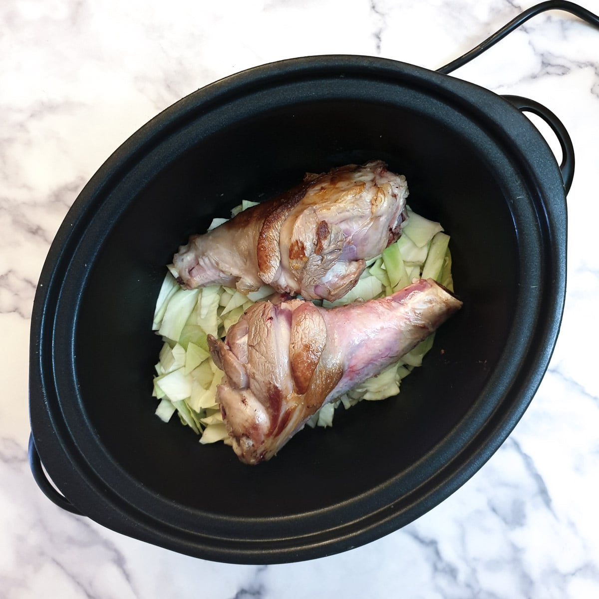 2 lamb shanks on a bed of shredded cabbage in a slow cooker.