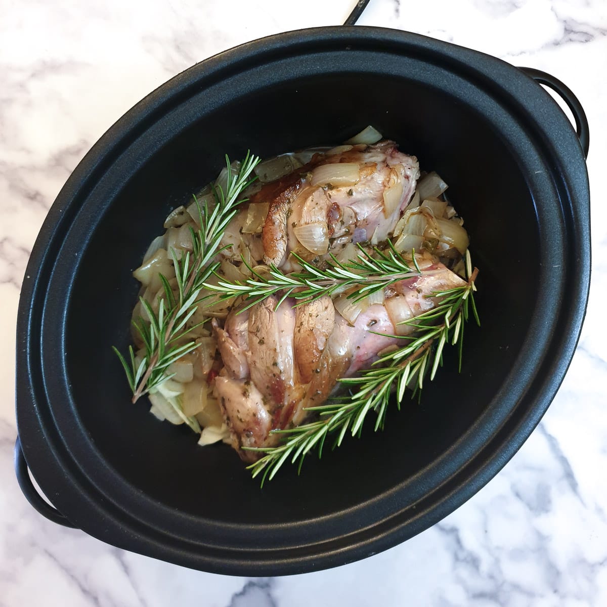 Lamb shanks in a slow cooker, topped with sprigs of rosemary.