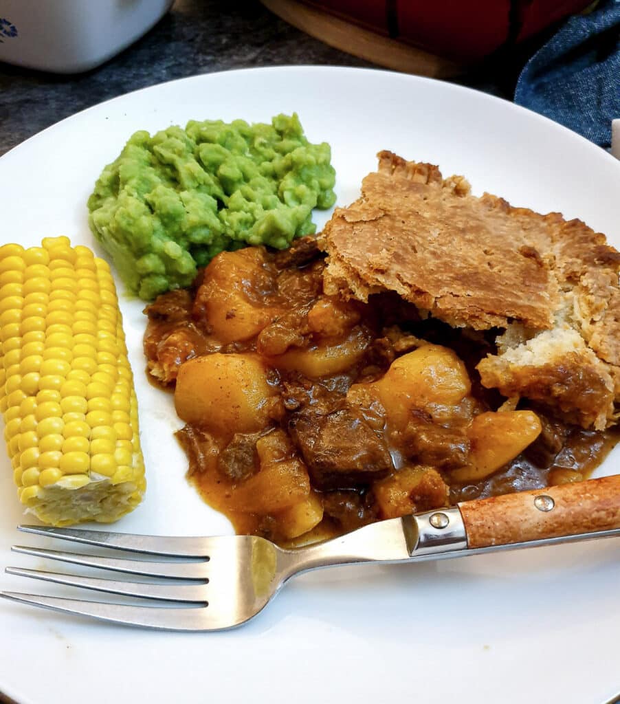 A helping of meat and potato pie on a plate with vegetables.