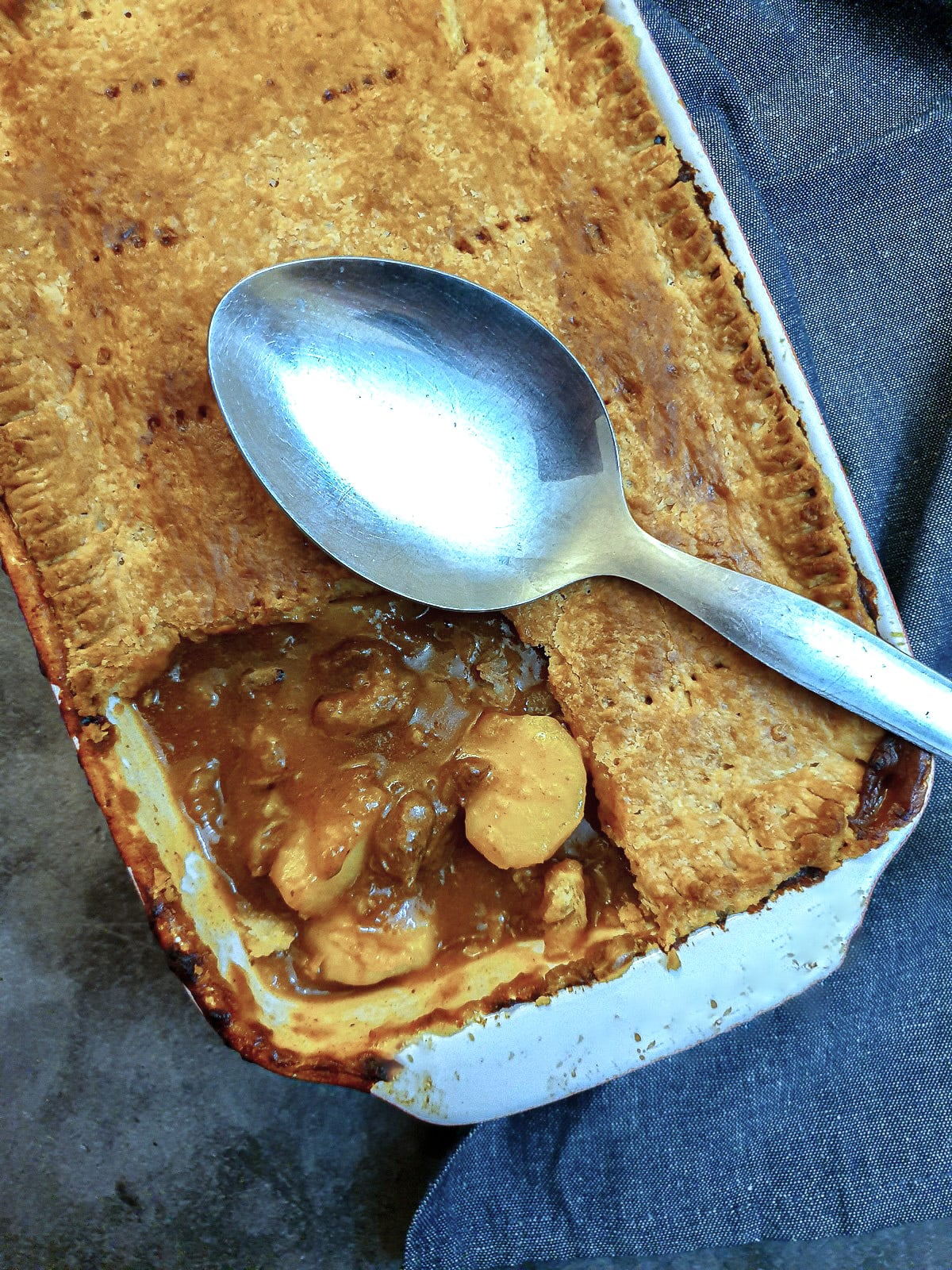 A meat and potato pie with one corner of the pastry cut away to show the filling.